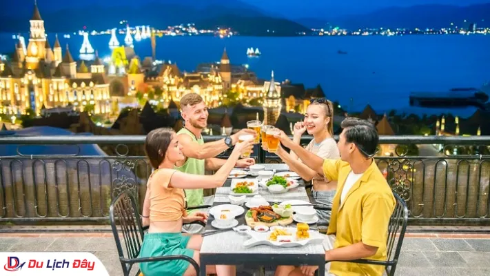 Nhóm du khách nâng ly ăn tối tại nhà hàng sân thượng lãng mạn hướng nhìn ra vịnh biển và lâu đài lên đèn
