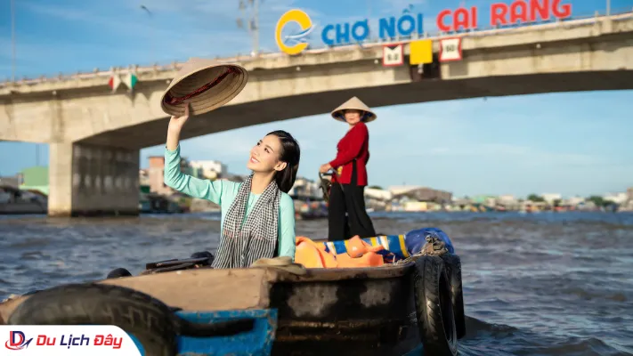 Du khách ngồi trên ghe trải nghiệm đội nón lá, check-in trước cây cầu có dòng chữ Chợ nổi Cái Răng miền Tây